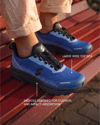 Feet wearing Silwer Active Ink Blue Men's Shoes on a wooden bench outdoors, with callouts for the large wide toe box and cushioned midsole