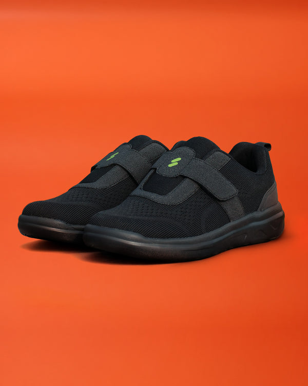 Pair of Silwer Ease Kohl Black Men's Shoes, angled view on an orange background showing the hook-and-loop strap and lightning bolt logo